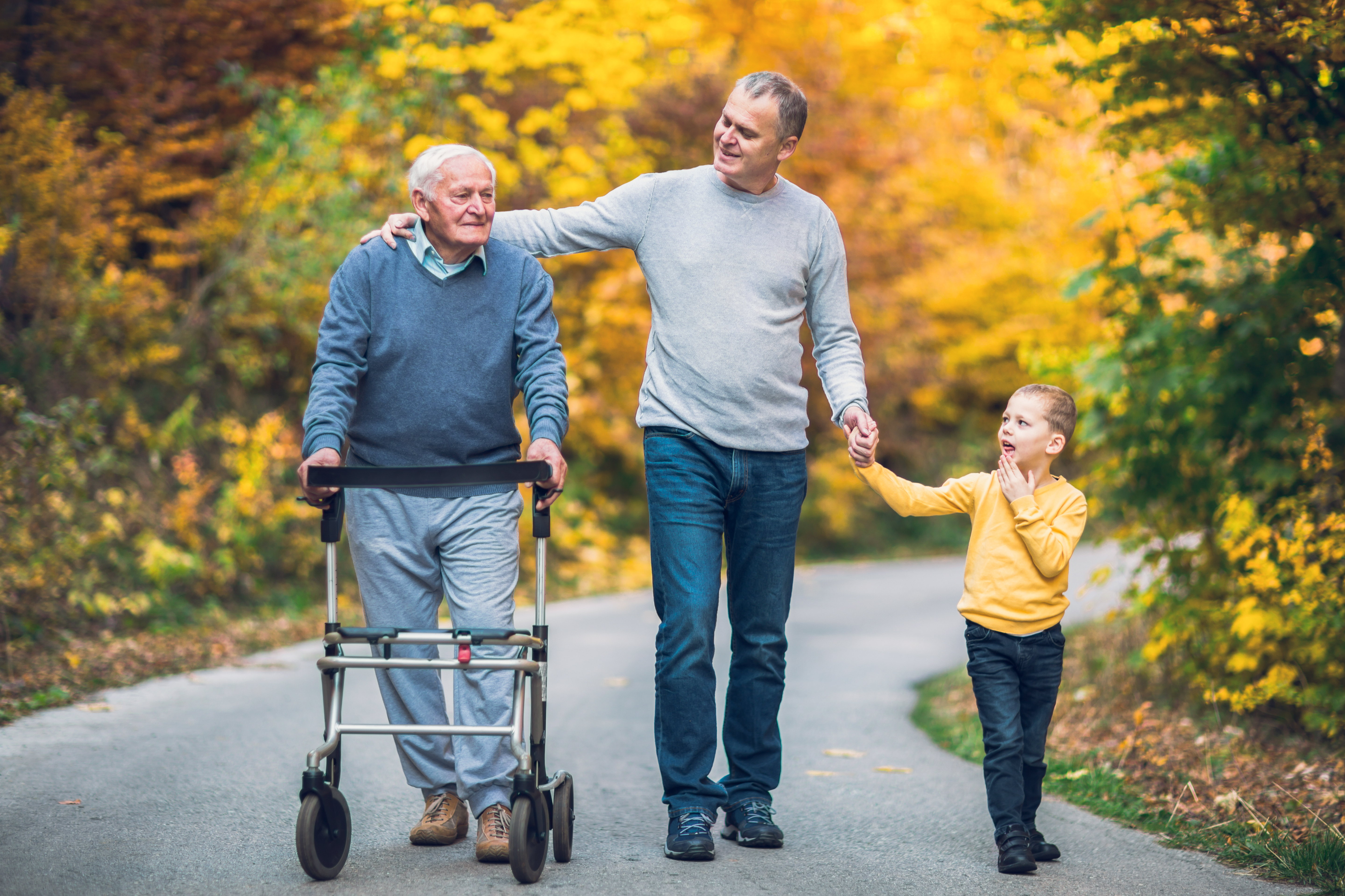 Drei Generationen beim Spaziergang: Großvater mit Rollator, Vater und Kind im herbstlichen Wald – ORTHOPARTNER Medizintechnik Porta